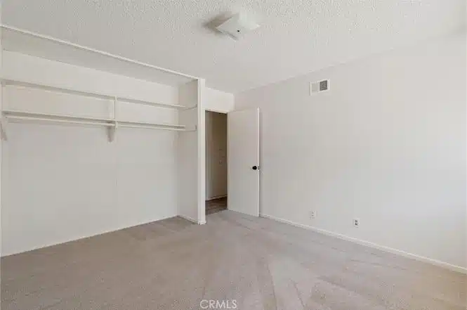 Empty room with carpet and open closet with shelves in California.